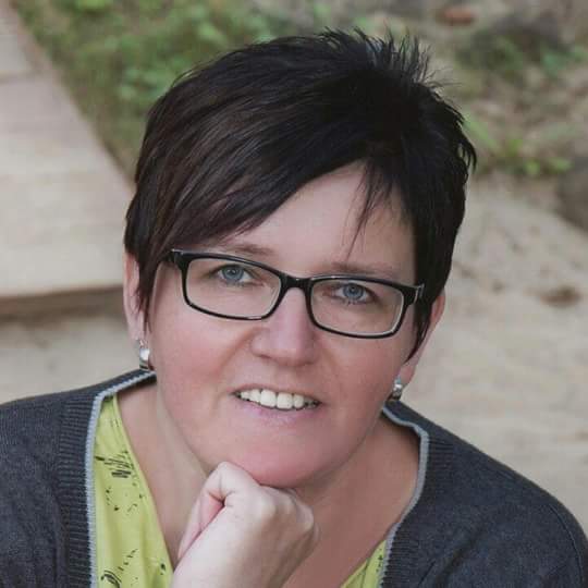 Ein Bild der Erzieherin Kerstin Nöcker. Sie hat kurze dunkle Haare und eine dunkel gerahmte Brille und lächelt auf dem Bild. 