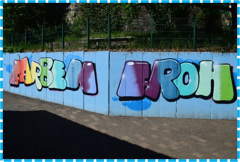 Auf dem Weg zur Kita ist der Schriftzug "Farbenfroh" in bunter Schrift aufgesprayt