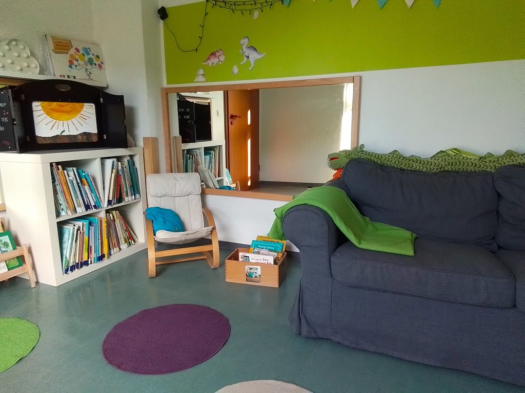 Die Leseecke mit bequemem Sofa, Regalen, Büchern und bunten Teppichen.